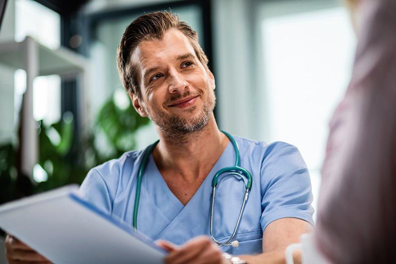 Happy doctor holding medical paperwork while communicating with patient during medical appointment at hospital. Happy doctor holding medical paperwork while communicating with patient during medical appointment at hospital.