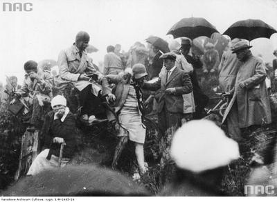 Kibice oczekujący w deszczu na przejazd samochodów.