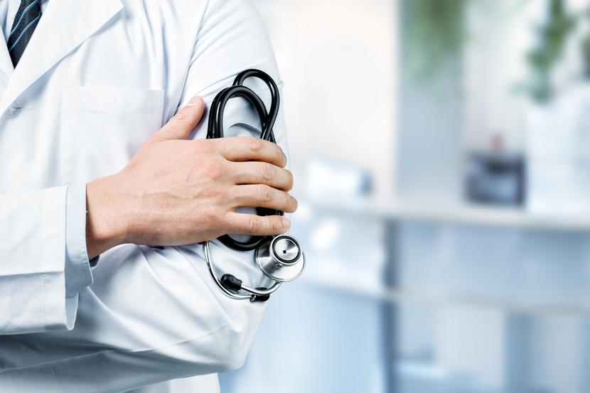 Young man doctor holding stethoscope on background